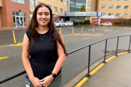 A student stands in front of a hospital building.